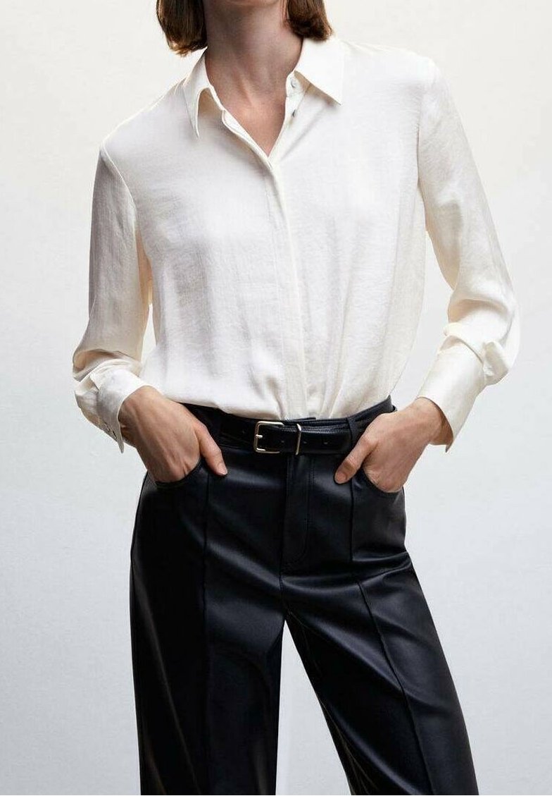Chemise blanche à manches longues avec col, associée à un pantalon en cuir noir taille haute et une ceinture noire. Texture lisse, coupe ajustée.