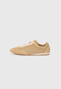Light brown sneaker made of suede and fabric, featuring a rounded toe, white laces, and a rubber sole with a textured finish.