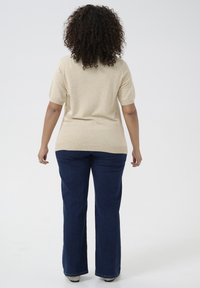 Beige short-sleeve sweater paired with dark blue wide-leg jeans. Soft texture, fitted at shoulders, casual style with a slight stretch.