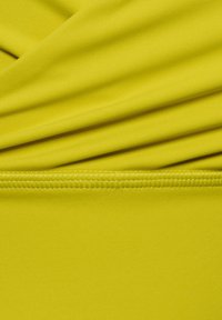 Skinnende gul stof med en glat tekstur, der har samlede plisseringer og en ren syet kant i bunden, der fremviser en ensfarvet farve.