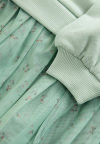 Mintgrøn kjole med en tætsiddende overdel med ribbede manchetter og en plisseret tylskørt, prydet med små blomster mønstre i pink og grøn.