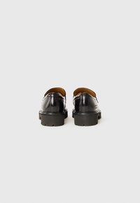 Scarpe in pelle nera con finitura liscia, punta arrotondata, dotate di una robusta suola in gomma nera e con accenti decorativi minimi.