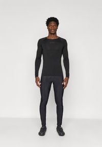 Czarna, długosleeve'owa, sportowa bluzka o dopasowanym kroju i okrągłym dekolcie, w połączeniu z czarnymi obcisłymi spodniami, obie części charakteryzują się gładką teksturą.