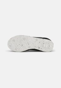 Black sneaker sole with a textured white rubber outsole featuring wave patterns and circular grips, showcasing detailed grooves and accents.