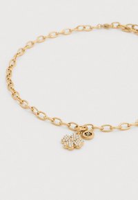 Κολιέ με αλυσίδα χρυσού που διαθέτει μενταγιόν τριφυλλιού με υφή, διακοσμημένο με καθαρά κρύσταλλα και μικρό γούρι με λογότυπο. Ρυθμιζόμενο μήκος.