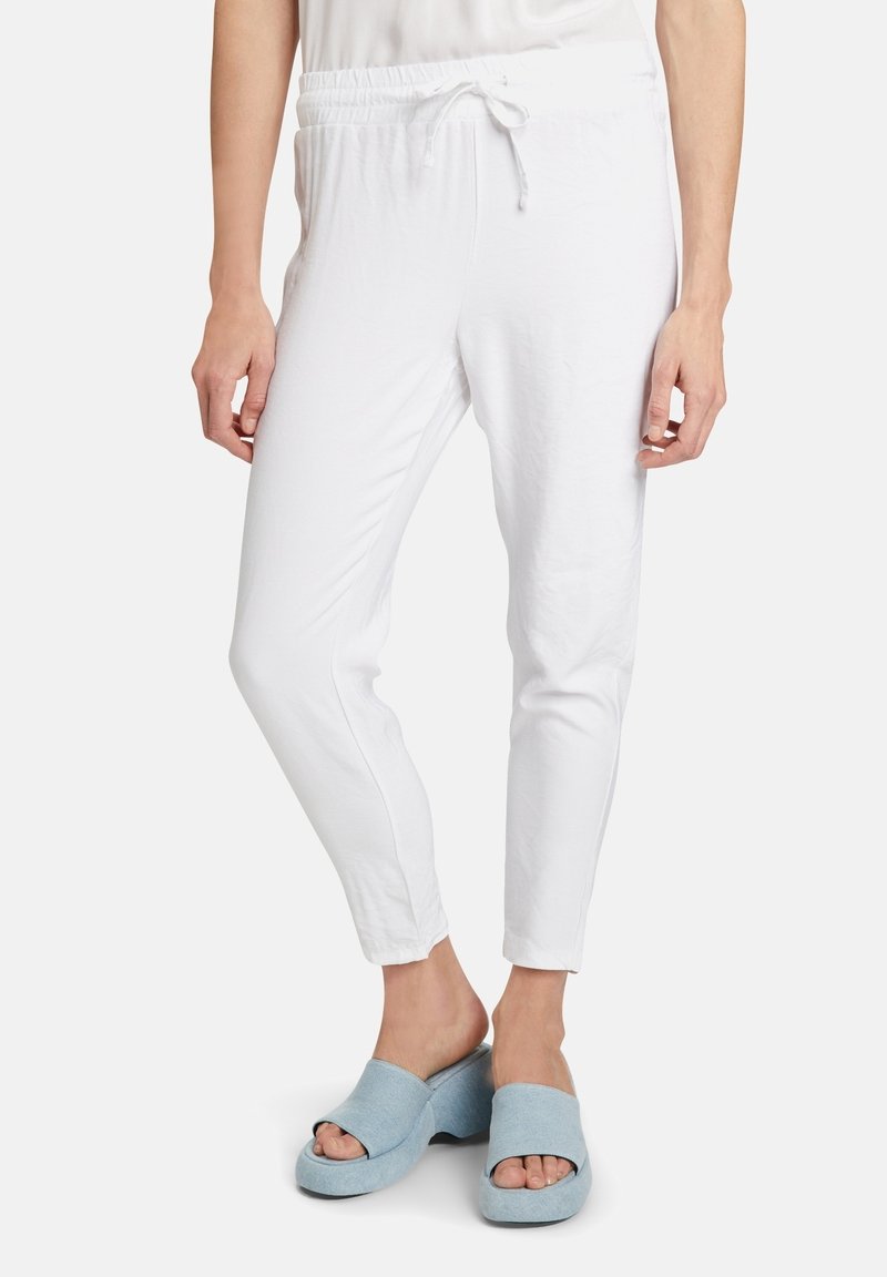 Bílé elastické kalhoty v pase s šňůrkou, s úzkým střihem, vyrobené z měkké látky. V kombinaci s modrými nazouvacími sandály na širokém podpatku.