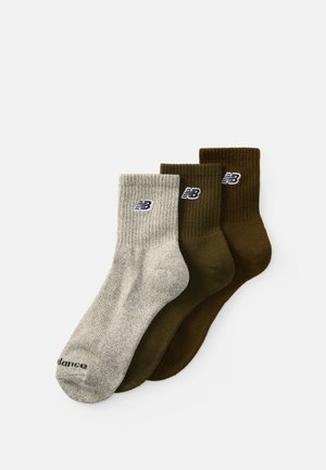 Trois paires de chaussettes montantes : une grise clair côtelée, deux solides vert foncé et marron, toutes avec un petit logo sur le revers.
