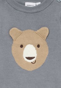 Grijze gebreide stof met een beige berengezicht met ronde oren, donkere ogen en een witte snuit met een glimlachende mond.