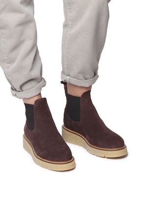 Botas de tobillo de ante marrón con paneles laterales de elastano y una suela de goma gruesa y de color claro. El caña tiene una textura suave y una punta redondeada.