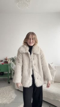 Šviesios smėlio spalvos dirbtinio kailio paltas su plačiu apykakliu, sagų užsegimu ir laisva siluete. Minkštos tekstūros, su ilgomis rankovėmis ir šoninėmis kišenėmis.