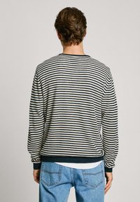 Sudadera de rayas en crema y azul marino, con mangas largas, puños acanalados y un escote redondo. Textura suave, corte holgado.