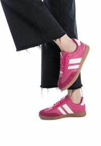 Le sneakers atletiche rosa presentano un mix di materiali lisci e testurizzati, con strisce bianche e una suola in gomma beige. Il design include una punta rotonda e un davanti con lacci.