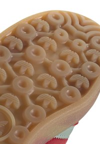 Semelle de chaussure en matériau en caoutchouc translucide texturé de couleur beige. Présente des motifs circulaires et des nervures pour la traction, avec un bord lisse.