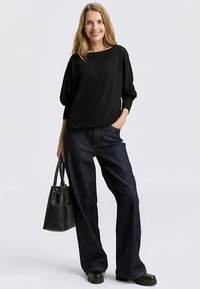 Black, loose-fitting sweater with a wide neckline paired with dark blue, high-waisted denim jeans and chunky black platform shoes. Carrying a black handbag.