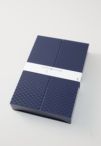 Tengerészkék ajándékdoboz, textúrált felülettel, fehér címkével, amelyen a "TOMMY HILFIGER" márkanevének van helye, öt pár terméket tart biztonságosan.
