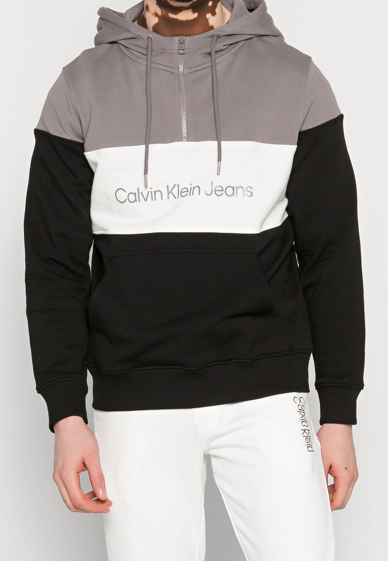 Sweat à capuche gris, blanc et noir avec fermeture éclair, doté d'une poche frontale et du logo « Calvin Klein Jeans » sur la poitrine. Texture douce.