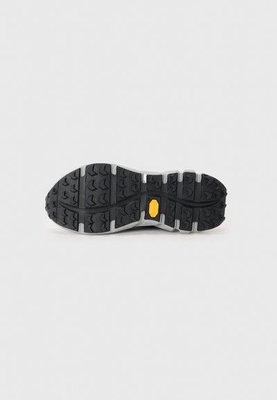 Black rubber shoe sole with deep treads, light gray accents, and a yellow Vibram logo, designed for traction and durability.