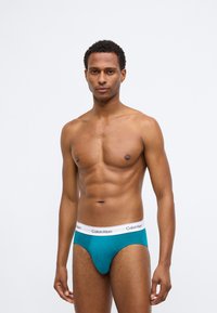 Tyrkysové bavlnené nohavičky s bielym pásom, na ktorom je čierne logo "Calvin Klein". Majú priliehavý strih a hladkú textúru.