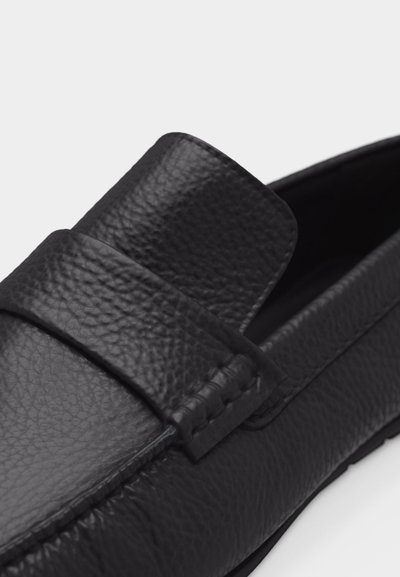 Mocassino in pelle nera con effetto granuloso, punta rotonda, dettaglio con cinturino cucito sulla parte superiore e tacco basso.