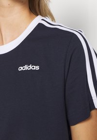 Camiseta de algodón azul marino con detalles en blanco, con cuello redondo acanalado y un diseño clásico de tres bandas en los hombros. Logo de adidas visible.