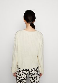 Maglione a coste crema con spalle scese, maniche ampie e vestibilità rilassata, abbinato a pantaloni a motivi bianco e nero.