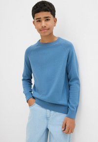 Maglione blu a maglia con collo a giro e polsini e orlo a costine. Indossato con jeans azzurri chiari, caratterizzati da una vestibilità rilassata e tasche laterali.