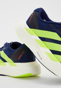Pantofii de alergare de culoare bleumarin au accente și dungi verzi, un material texturat pentru partea superioară și o talpă intermediară albă cu marcaj "LIGHTSTRIKE PRO".