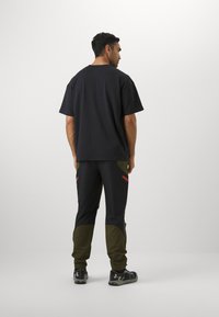 T-shirt noir à coupe ample associé à un pantalon noir et vert olive avec des accents rouges et des poches, conçu pour le sport.