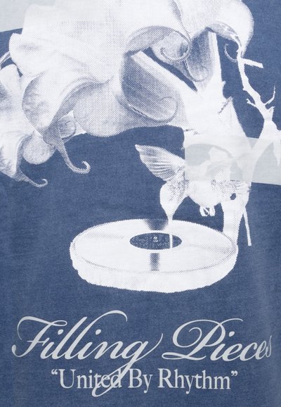 Graphic t-shirt with a blue background featuring a white illustration of flowers and a record player, including text: "Filling Pieces 'United By Rhythm'."
