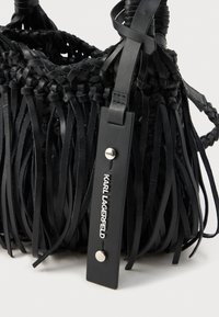 Czarna torebka z plecionego skóry z długimi frędzlami. Posiada solidny skórzany pasek z srebrnym ćwiekiem i metalową tabliczką z logo marki.