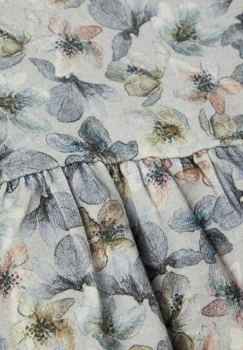 Tissu doux avec un motif floral discret comprenant des fleurs bleues, roses et beiges sur un fond clair avec des fronces.