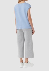 Helles blaues Kurzarm-Oberteil mit geradem Schnitt, kombiniert mit grauen weit geschnittenen Jogginghosen und weißen Sportschuhen. Einfaches und lässiges Design.