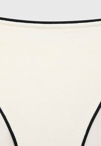 Beige thong underwear with a textured surface and a contrasting black elastic waistband. The edges are stitched for durability.