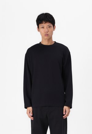 Black long-sleeve shirt made of soft material, featuring a round neckline and relaxed fit, paired with dark pants.