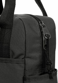 Kompaktní černý látkový batoh s texturovaným povrchem, zipy a boční kapsou. Obsahuje pevné rukojeti a zesílené švy.