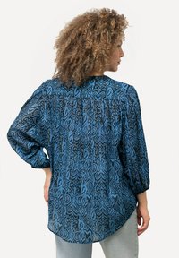 Blusa blu a fantasia con maniche lunghe, caratterizzata da una vestibilità morbida e un orlo curvato. Il materiale ha un aspetto texturizzato e leggero.