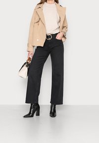 Beige trench coat, light textured top, black wide-leg jeans, black crocodile-embossed ankle boots, and small black and cream handbag.