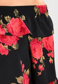 Black fabric with large red rose floral print and elasticized ruffled waistband on a garment.