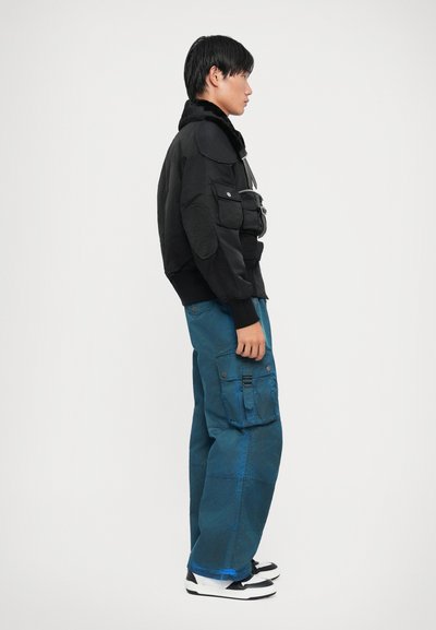 Musthave musta bomberjakk, millel on karvane krae, kombineeritud lõdva teal värvi cargo-pükste ja küljepocketite ning rihma detailidega. Mustad ja valged tossud.