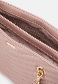 Borsa trapuntata rosa con una texture liscia, dotata di accessori dorati e una targhetta con il logo, e più scomparti interni per l'organizzazione.