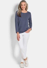 Gestreiftes Longsleeve-Shirt in Marineblau und Weiß, kombiniert mit weißen Hosen und hellen Sneakers, mit Rundhalsausschnitt und lockerer Passform.
