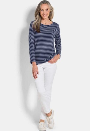 Gestreiftes Longsleeve-Shirt in Marineblau und Weiß, kombiniert mit weißen Hosen und hellen Sneakers, mit Rundhalsausschnitt und lockerer Passform.