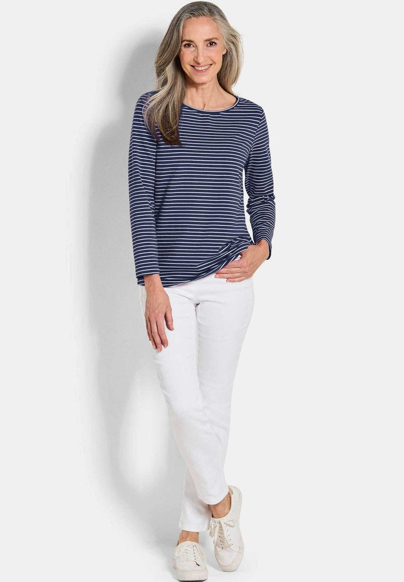 Gestreiftes Longsleeve-Shirt in Marineblau und Weiß, kombiniert mit weißen Hosen und hellen Sneakers, mit Rundhalsausschnitt und lockerer Passform.