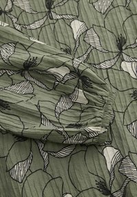 Zielona tkanina z wzorem kwiatowym w czarnych konturach i białych akcentach. Teksturowana powierzchnia z widocznymi plisami.