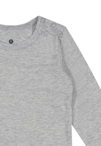 Lys grå langærmet skjorte lavet af blødt stof. Har rund halsudskæring med trykknapper på skulderen for nem påklædning.