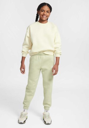 Un sweatshirt jaune clair avec un col rond, associé à un pantalon de survêtement vert clair doté d'une taille élastique. Des baskets dans des tons neutres.