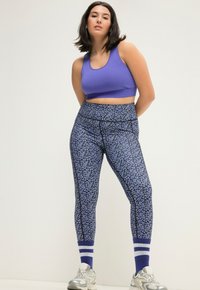 Paarse crop top met blauw en zwarte legging met een bloemenpatroon. Witte en blauwe gestreepte sokken maken de sportieve look compleet.