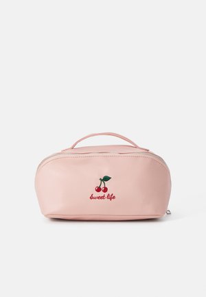 Bolsinha de cosméticos rosa com forma arredondada, material têxtil, design de cereja bordado e texto "vida doce", com fecho em zíper na parte superior e alça.