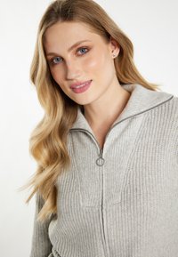 Maglione grigio con zip, caratterizzato da un motivo a maglia testurizzata, con colletto alto e zip circolare. Materiale morbido e caldo.