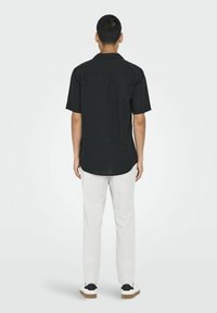 Camisa negra de manga corta con dobladillo recto, combinada con pantalones gris claro. La camisa presenta una textura suave y un corte relajado.